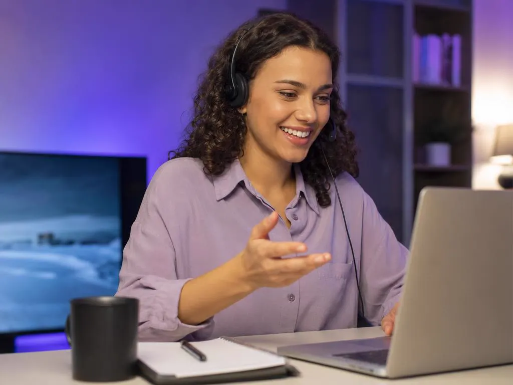 Smiling support agent with a headset helping a customer on a laptop