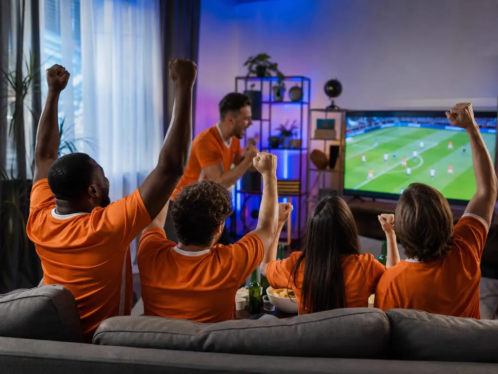 Friends in plain orange shirts cheering a soccer match on TV