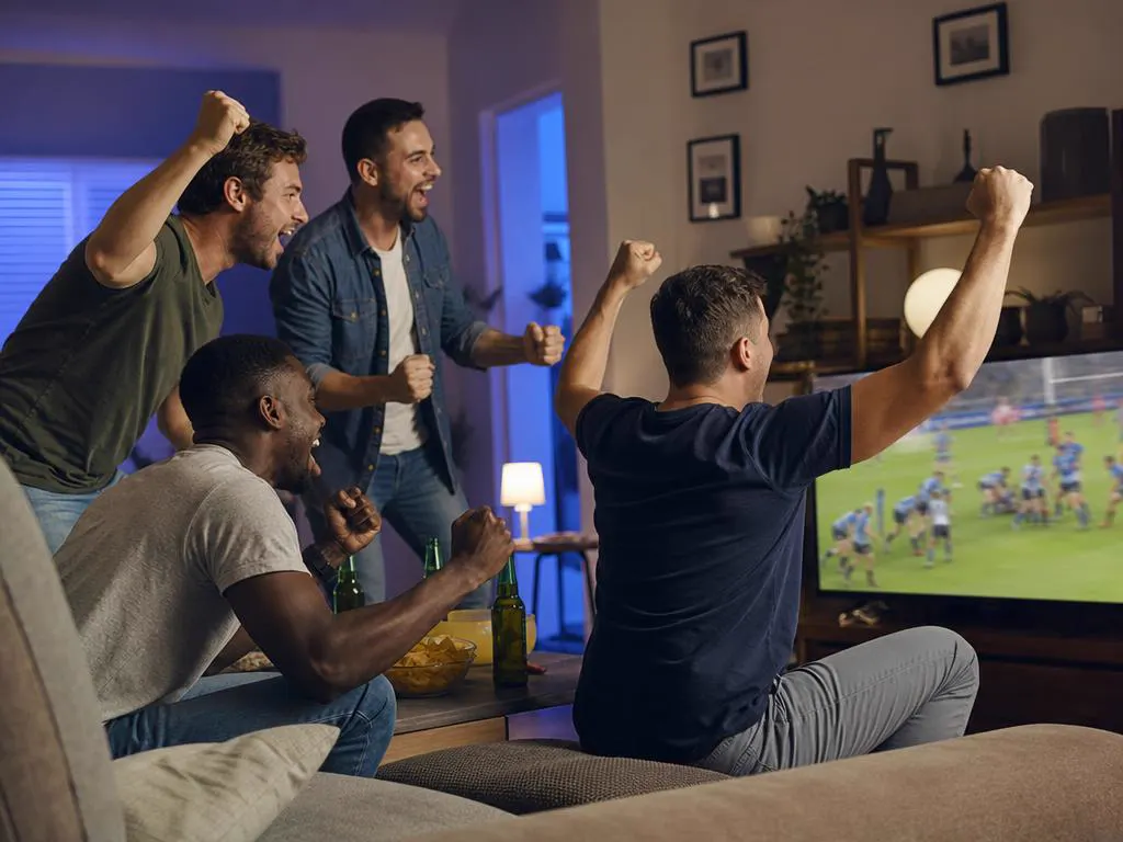 Friends cheering a rugby match on TV in a cozy apartment