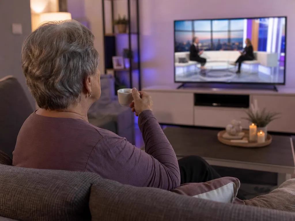 Grandmother with a coffee watching a Greek morning show on TV