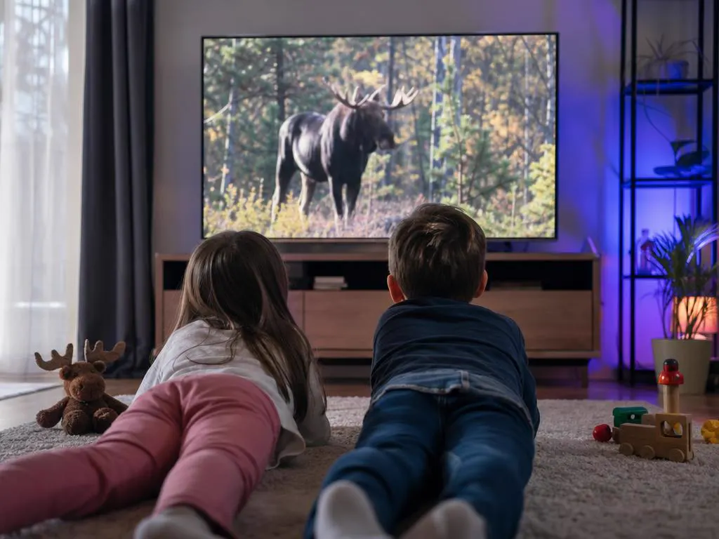 Two kids on a rug watching a bright wildlife documentary on a TV