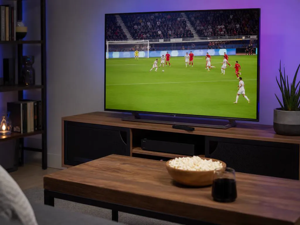 Fire TV Stick and remote on a media console beneath a TV showing a bright live sports game