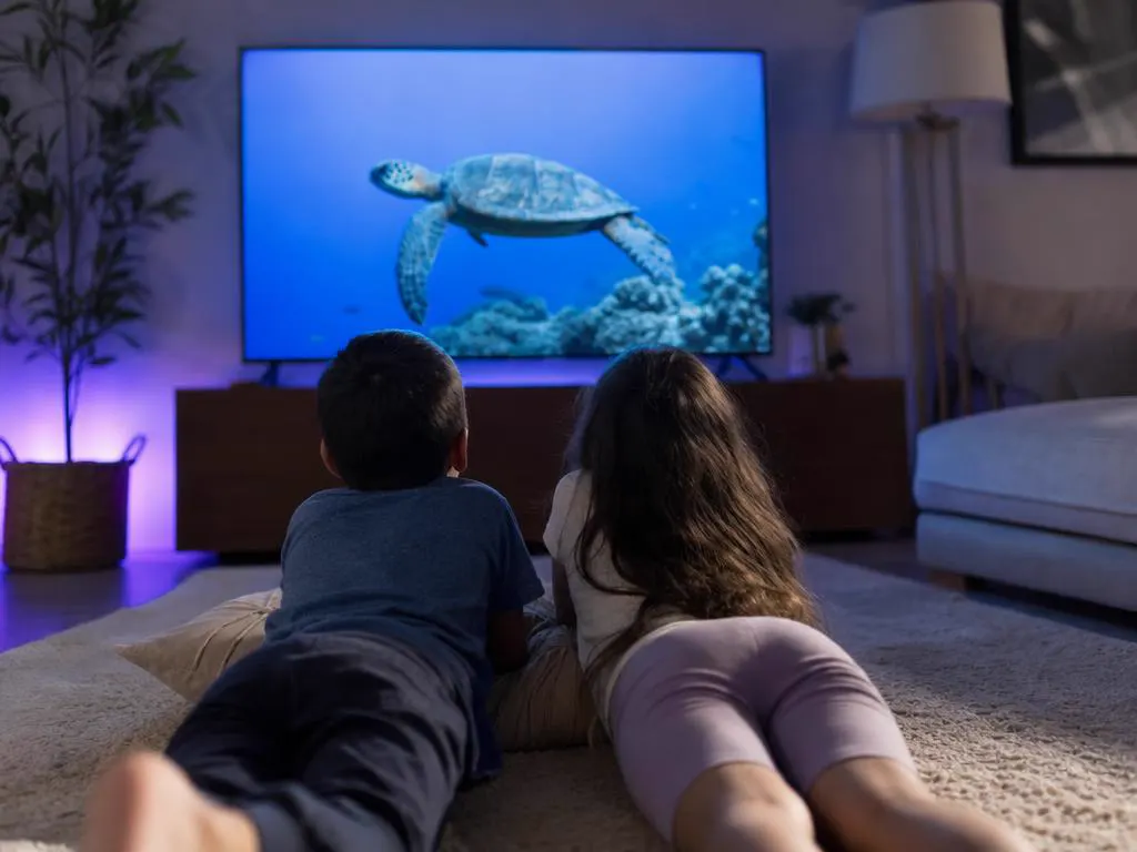 Enfants devant une émission nature avec des tortues de mer sur une grande TV