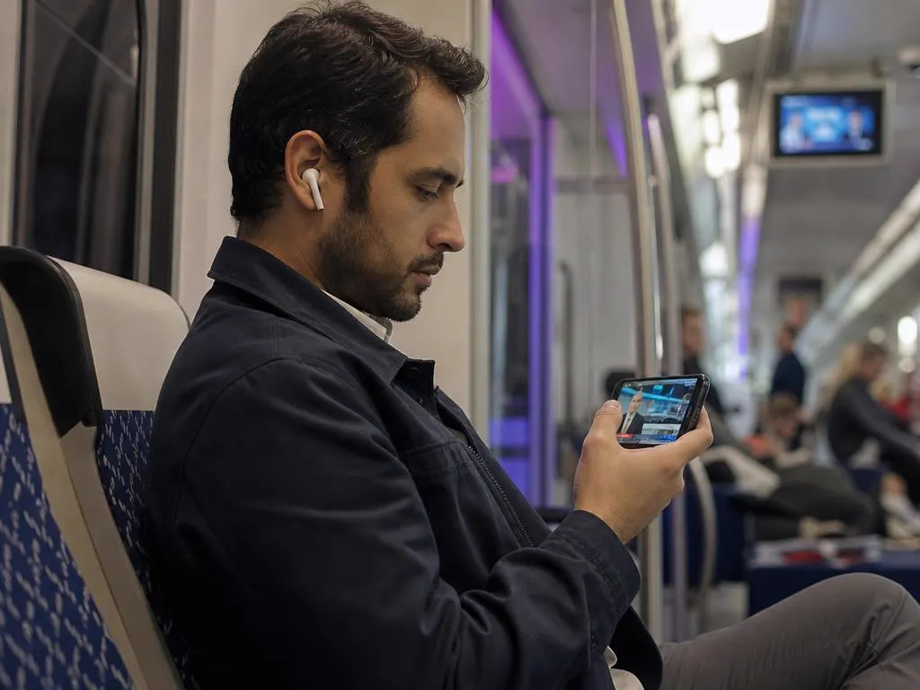 Voyageur dans un train qui regarde les infos en direct sur un iPhone avec des écouteurs