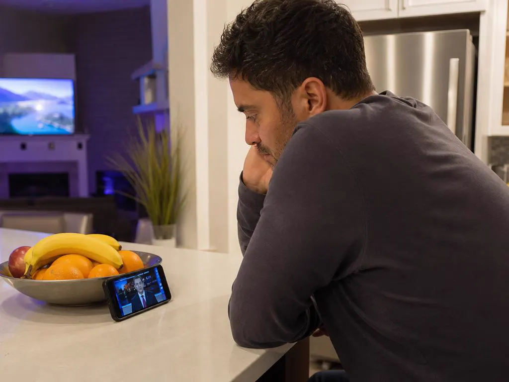 Homme qui regarde les infos sur un iPhone posé dans une cuisine
