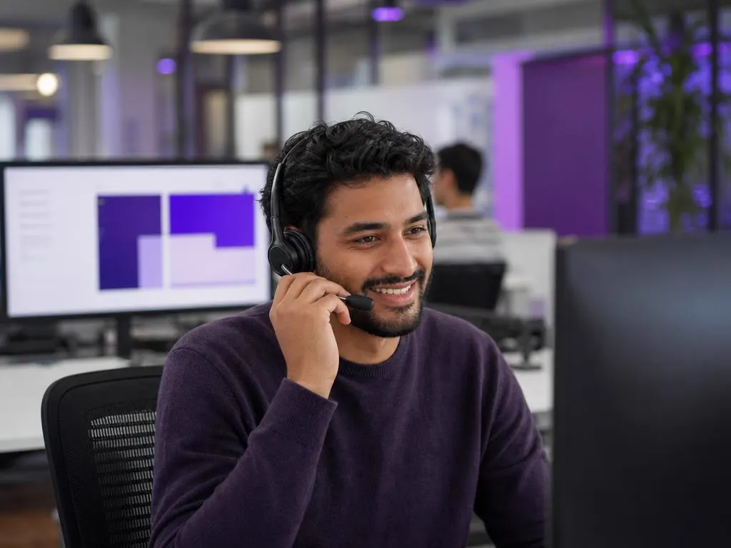 Conseiller support avec un casque qui aide un client au téléphone dans un bureau lumineux