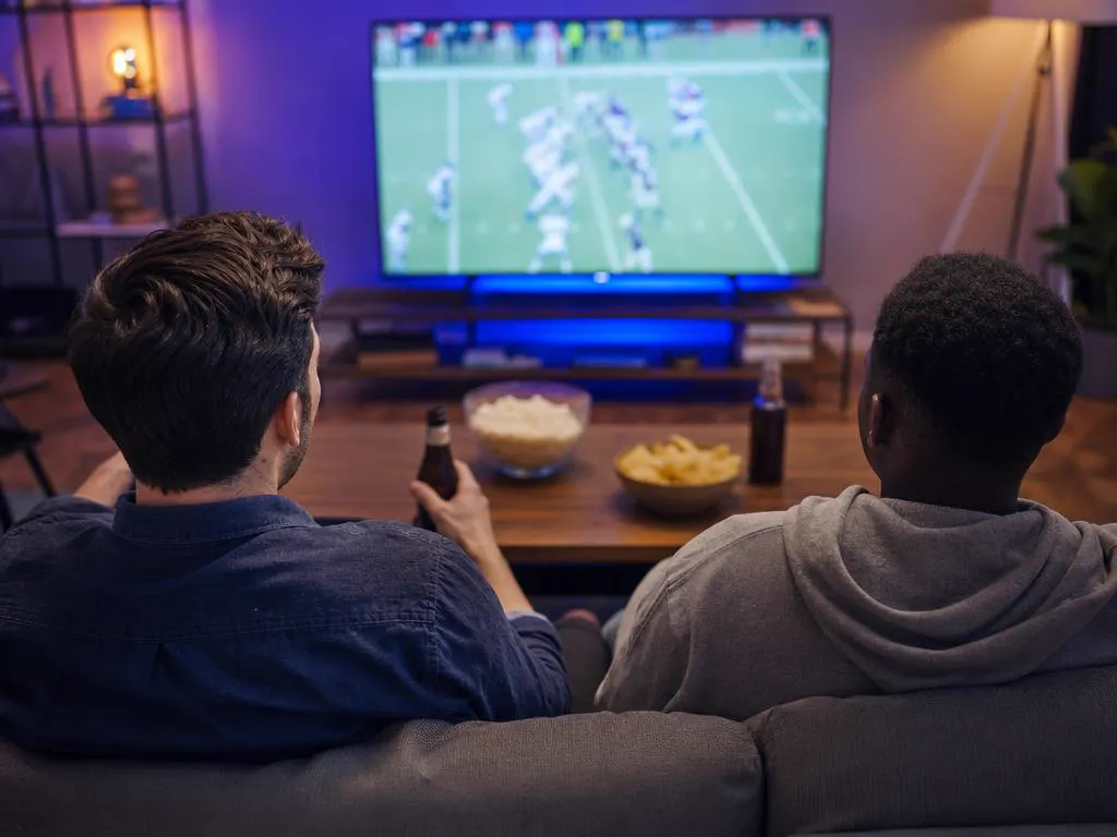 Deux amis devant un match en direct sur une Smart TV avec des encas
