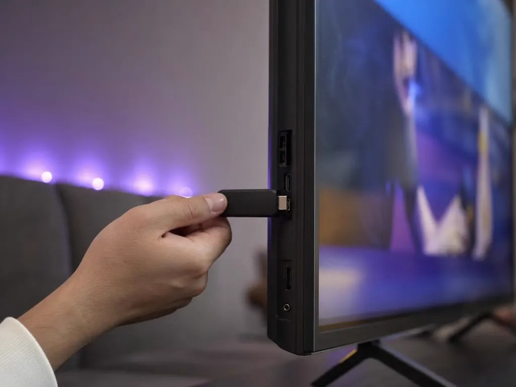 Main qui branche une clé de streaming sur le côté d’une Smart TV fine