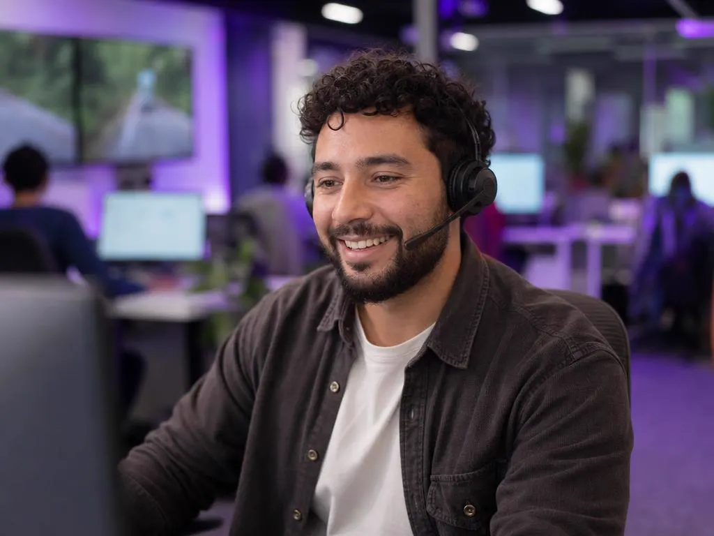 Smiling support agent with a headset helping a customer by phone in a bright office
