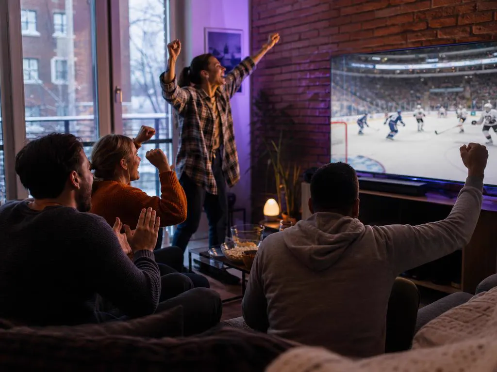Friends in a Montreal apartment cheering a hockey game on TV during a snowy evening