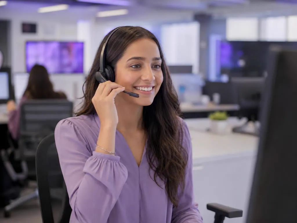 Smiling support agent with a headset helping a customer on a phone