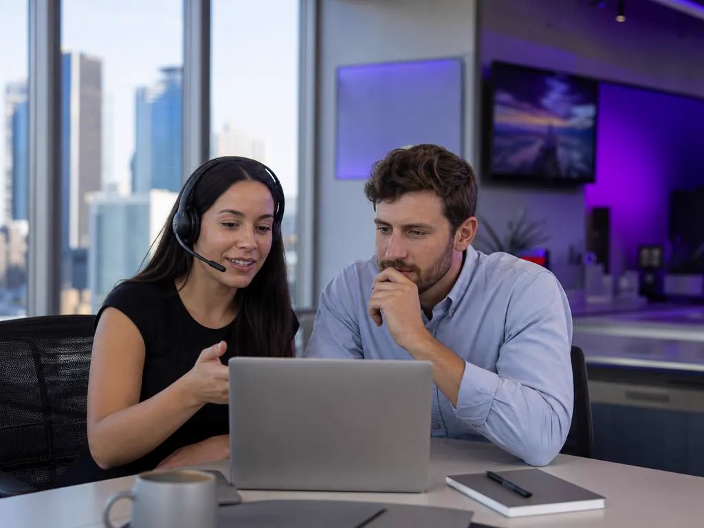Support specialist with a headset helping a customer on a laptop in a bright city office