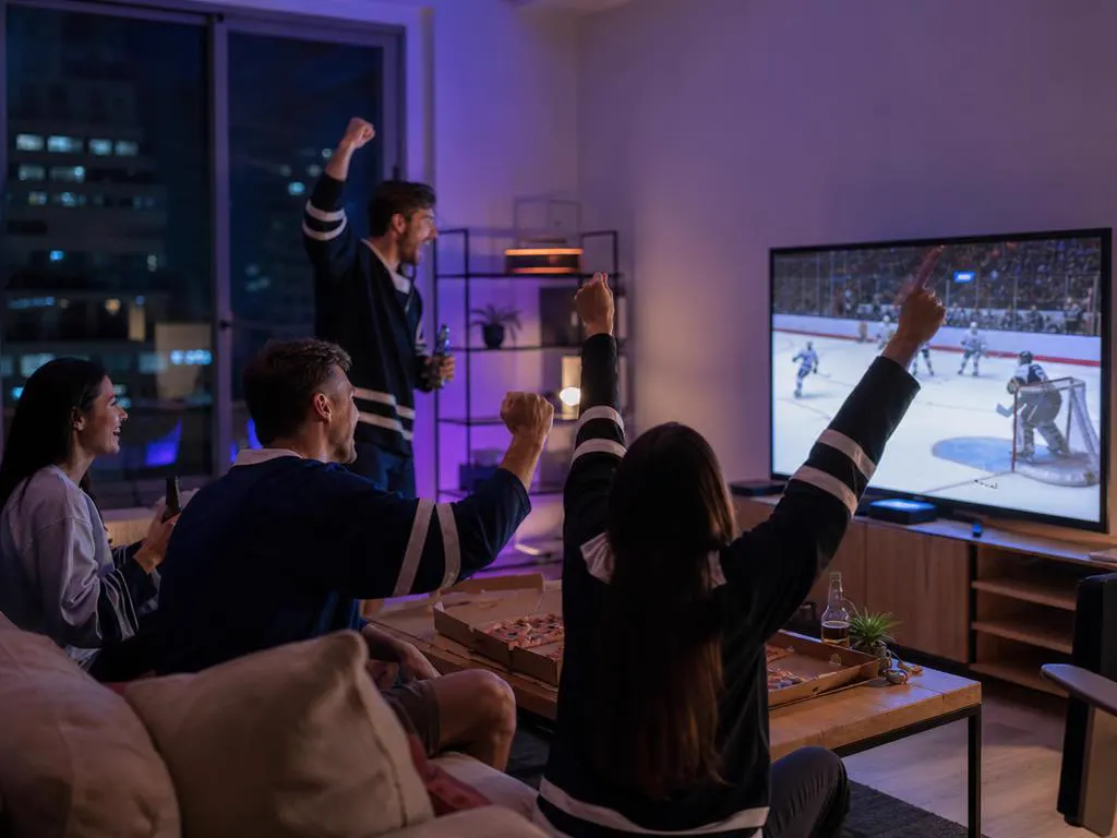 Group of friends in a downtown apartment watching a hockey game on a large TV at night