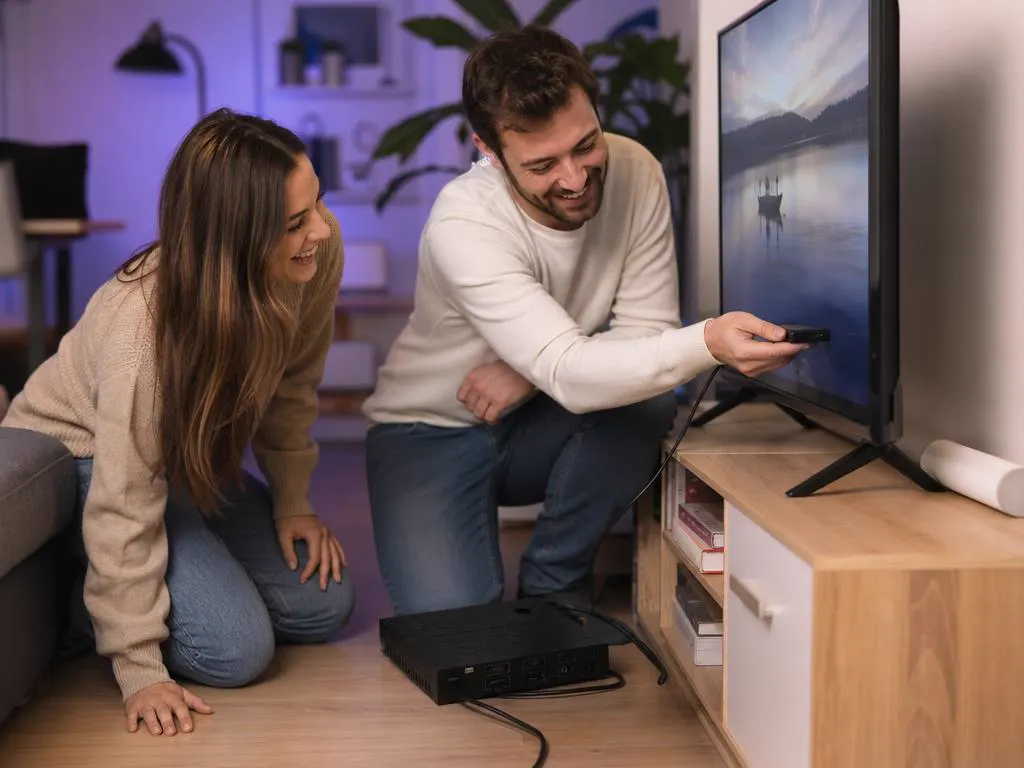 Couple setting up a streaming stick on a TV, a cable box unplugged on the floor