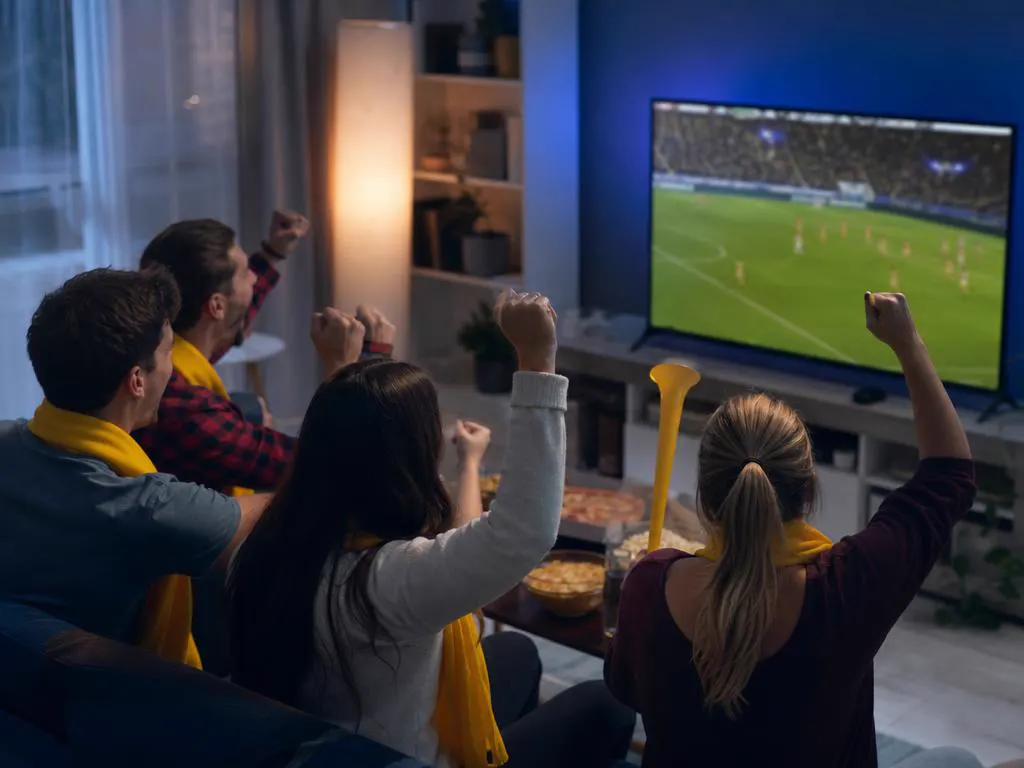 Amis avec des écharpes jaunes qui encouragent une équipe de football à la TV