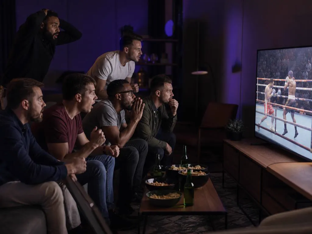 Amis réunis autour d’une TV pour un combat de boxe dans un salon tamisé