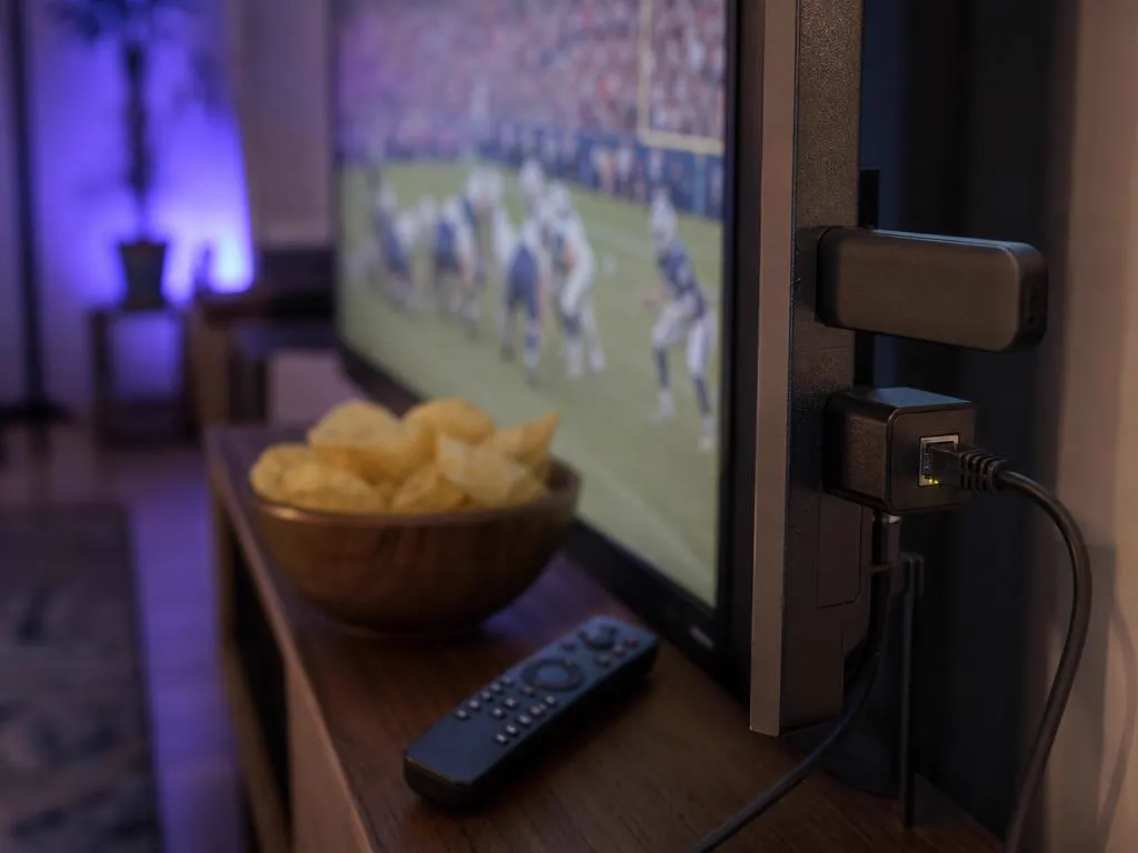 Clé de streaming et adaptateur Ethernet branchés sur une TV avant un grand match, télécommande sur la table
