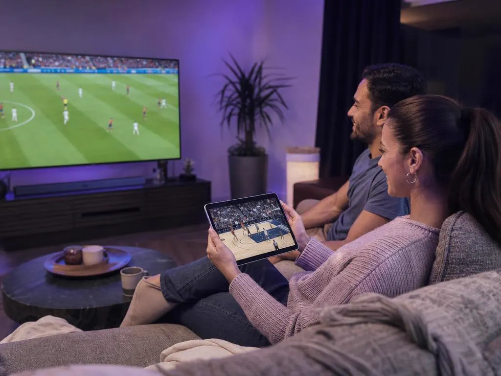 Salon avec deux personnes devant deux matchs différents, l’un sur la TV et l’autre sur une tablette