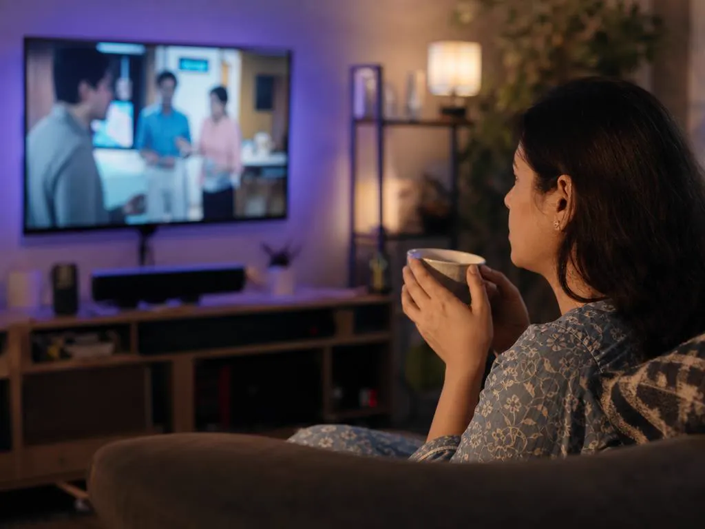 Femme devant une série du soir à la TV avec une tasse de thé